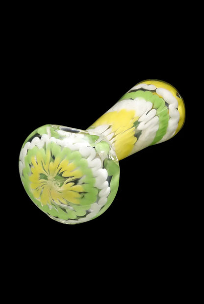 Angled close-up of the Smoke Cartel Fancy Multi-Color Striped Glass Spoon Pipe - 5 in. showing its green, yellow and white swirled floral pattern against a black background