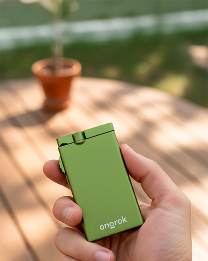 Handheld three-quarter view of an ONGROK Aluminum Dugout in green held over a sunlit wooden table with a blurred potted plant in the background