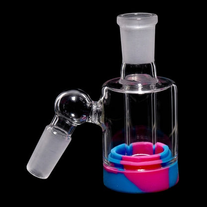 Close-up angled view of the Smoke Cartel 3.5-inch Silicone Base Reclaim Ash Catcher - 45 degree - 14mm showing its clear glass joint and frosted connector above a blue-and-pink silicone base against a black background.