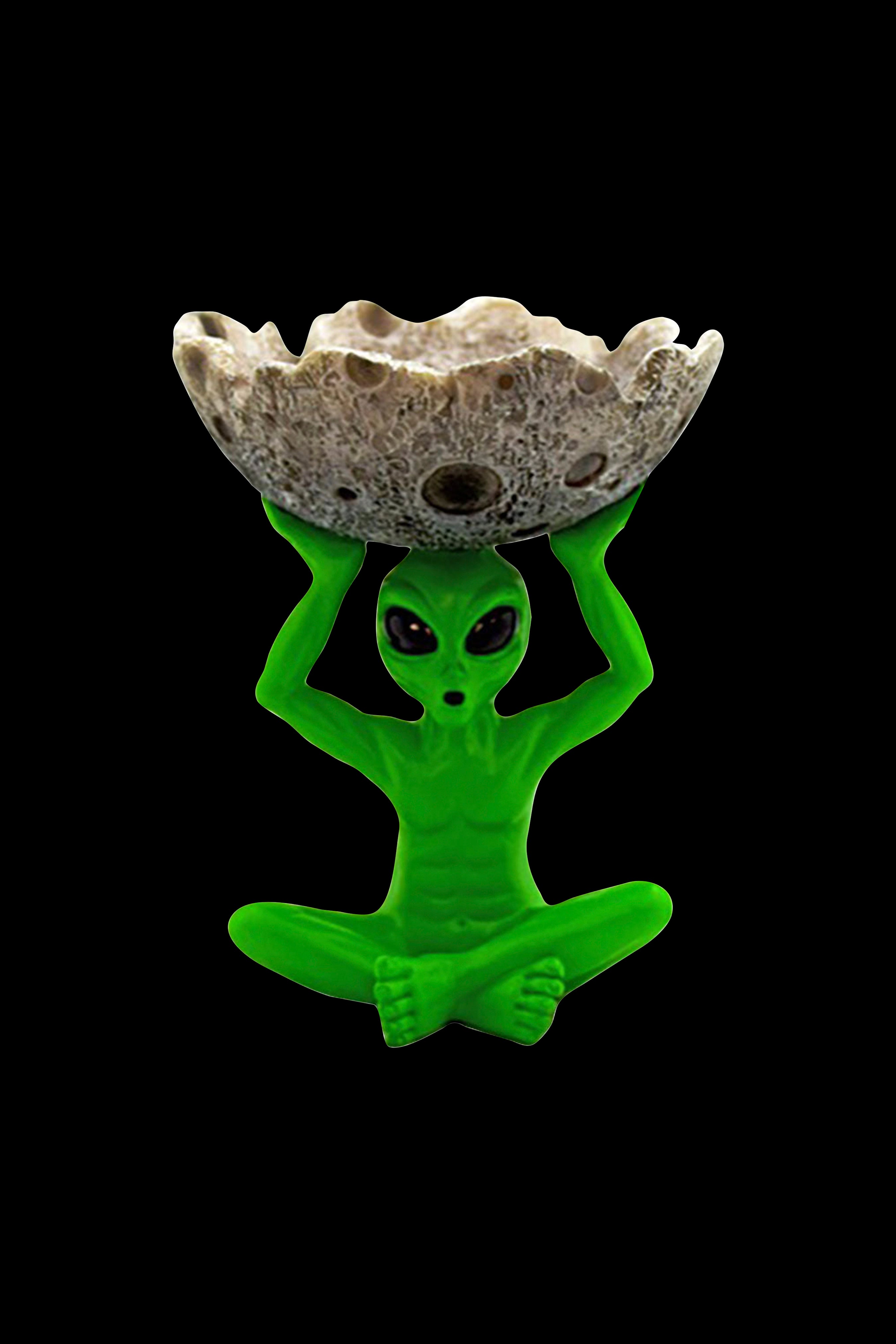 Green alien sculpture holding a speckled stone ashtray or catch-all, isolated on black.
