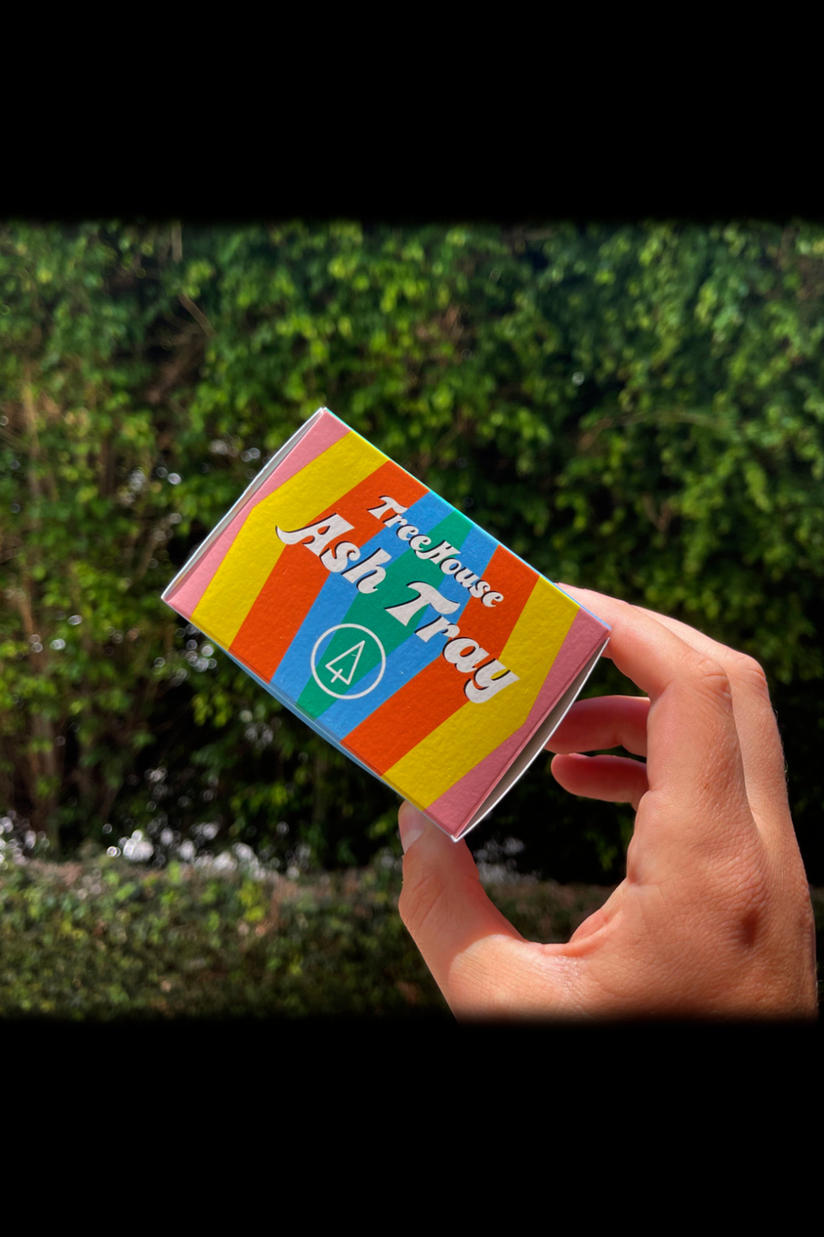 Hand holding a pink “Treehouse Ash Tray” against a blurred green foliage background.