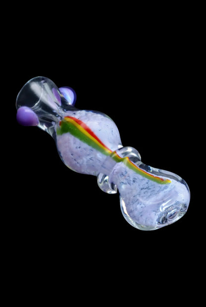 Angled close-up of the Smoke Cartel Frit Rasta One Hitter - 3 in. glass piece showing a purple-speckled body with a red-yellow-green rasta stripe and purple accents on a black background