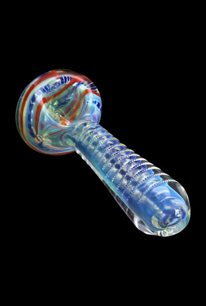 Angled close-up of the Smoke Cartel Engraved Fumed Spoon Pipe - 3 in., showing a ribbed translucent blue stem and swirled multicolor bowl on black.