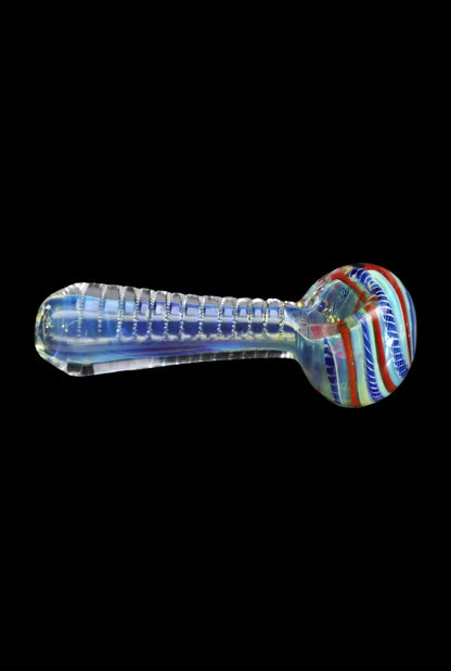 Side view of the Smoke Cartel Engraved Fumed Spoon Pipe - 3 in., showing a clear fumed glass body with ribbed engraving and a colorful striped bowl against a black background