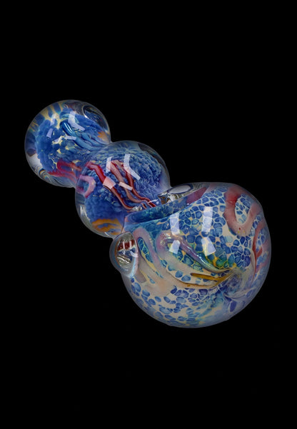 Angled close-up of the Smoke Cartel Fancy Frit Spoon Pipe - 3.5 in. showing swirled blue frit, pink ribbon accents, and glossy reflections on a black background