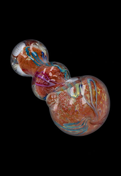 Angled close-up of the Smoke Cartel Fancy Frit Spoon Pipe - 3.5 in., showing orange frit clusters and blue ribbon-like swirls beneath clear glass on a black background