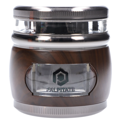 Close-up front view of the Smoke Cartel Glossy 3-Stage Grinder - 62mm showing its reflective gunmetal top, clear middle chamber, and wood-toned base with a small clear window.