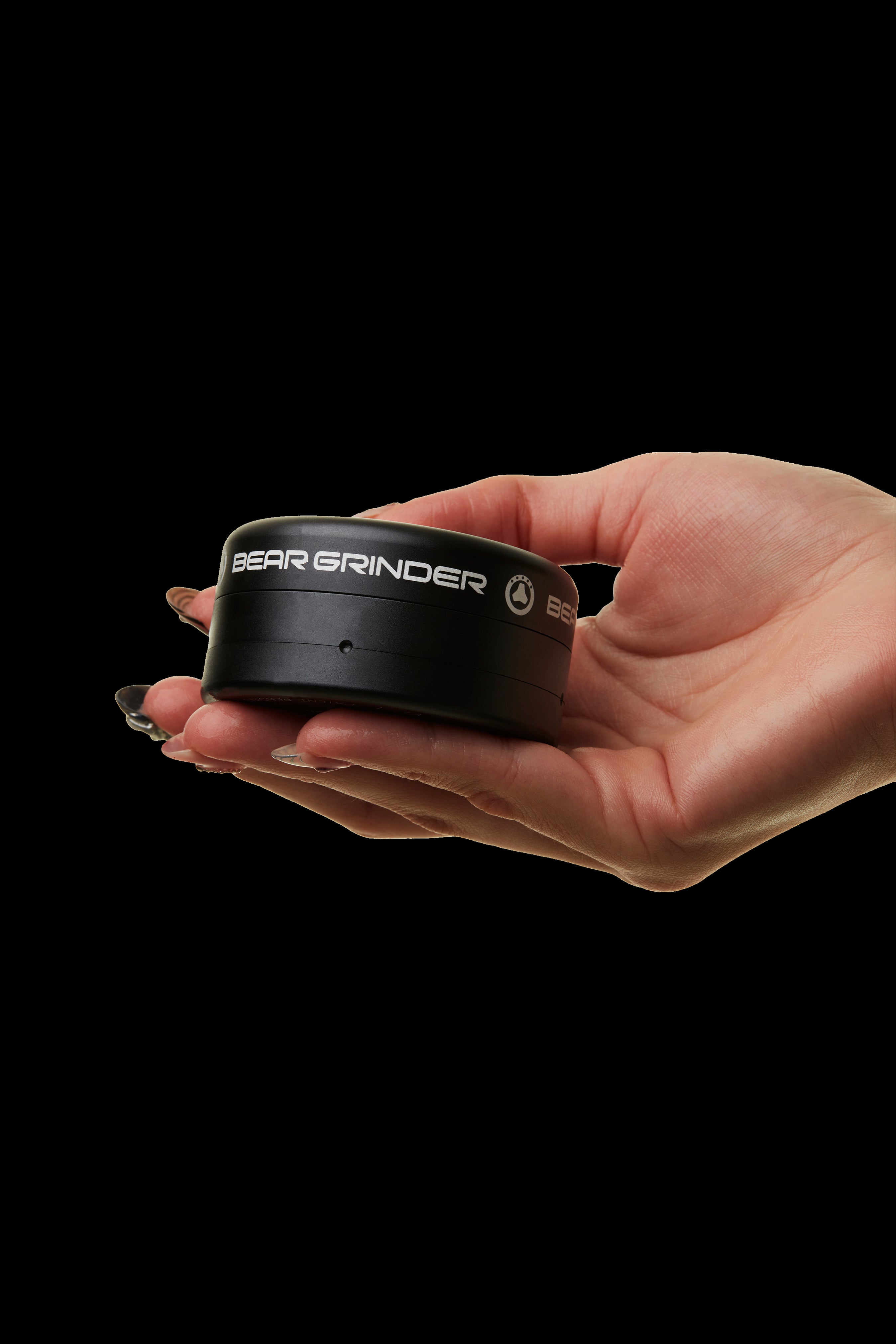 Black cannabis grinder held in a hand against a dark background.