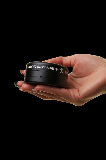 Black cannabis grinder held in a hand against a dark background.