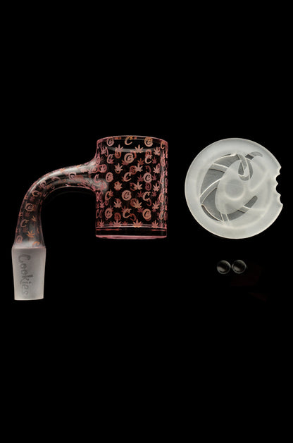 Pink glass cannabis bubbler with leaf patterns, alongside a glass bowl and two small glass beads, all against a black background.