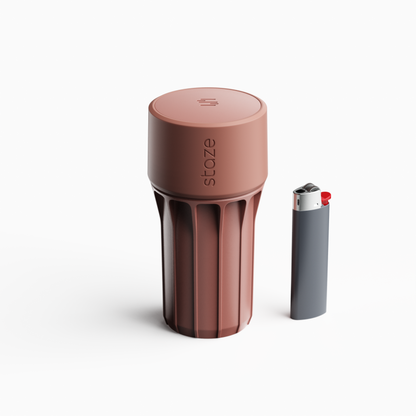 Close-up front view of the rose‑tan STAZE PRESERVE cylinder showing its textured top and vertical grooves beside a slim lighter.