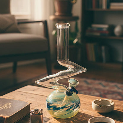 Front three-quarter view of the La Pipes Z-Shape Bubble Bong - Zig Zag Percolator sitting on a wooden table with warm window light highlighting its clear zigzag neck and swirled glass bubble base.