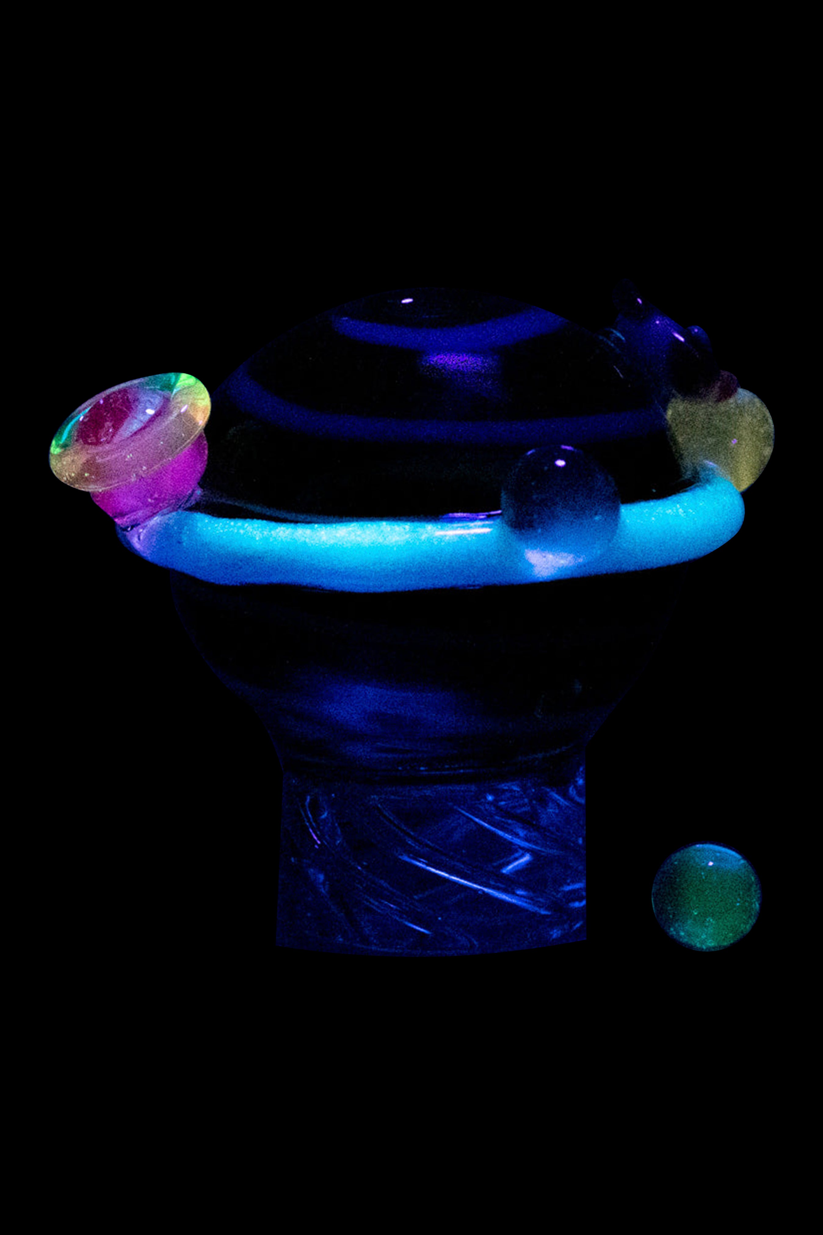 Glow-in-the-dark glass cannabis water pipe with colorful accents against a black background.