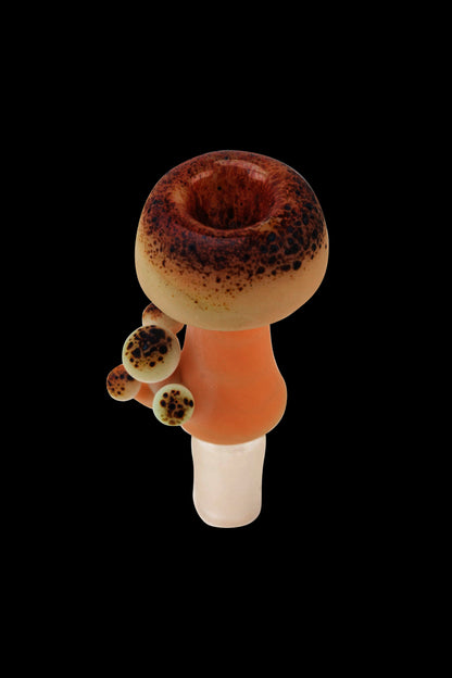 A vibrant glass pipe with a mushroom-inspired design, featuring a speckled brown and cream cap and orange stem, against a black background.
