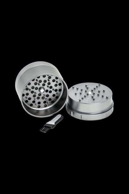 Silver cannabis grinder disassembled with included scraper tool, isolated on a black background.