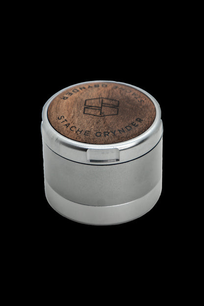 Silver cannabis grinder with a wooden top engraved with a logo.