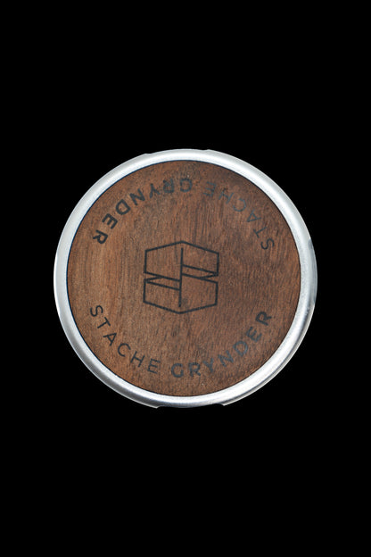 Wood and silver cannabis grinder with “Stache Grinder” engraved around a geometric logo.