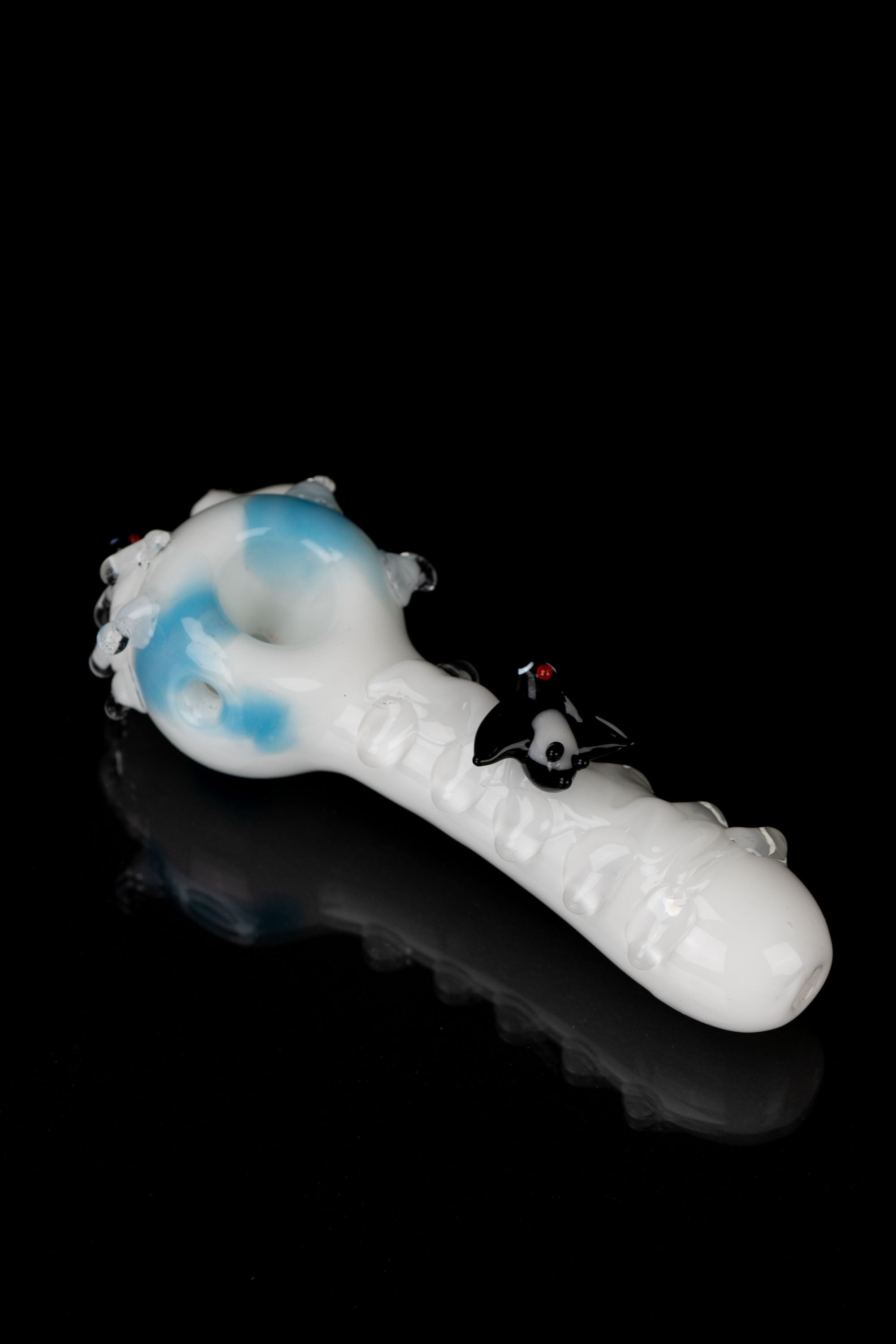 Glass pipe with blue and white swirling patterns, featuring a sculpted black skull detail, on a reflective black surface.