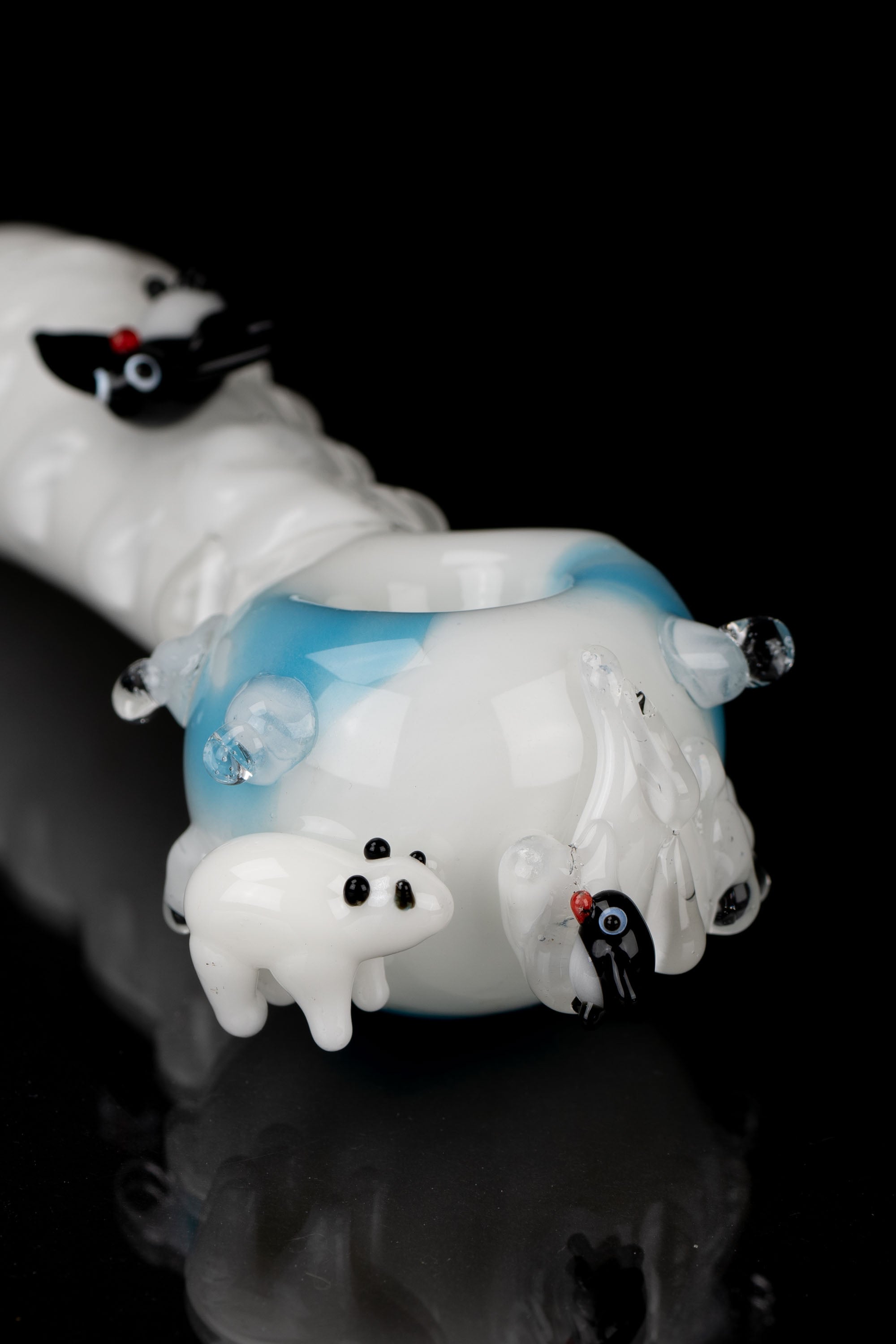 A whimsical glass pipe shaped like a melting snowman with a blue top hat and red eyes, against a black background.