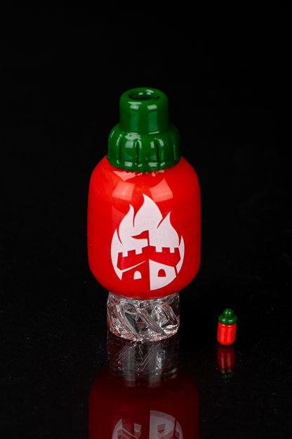 Red glass dab rig shaped like a chili pepper with a green cap, reflecting on a textured surface.