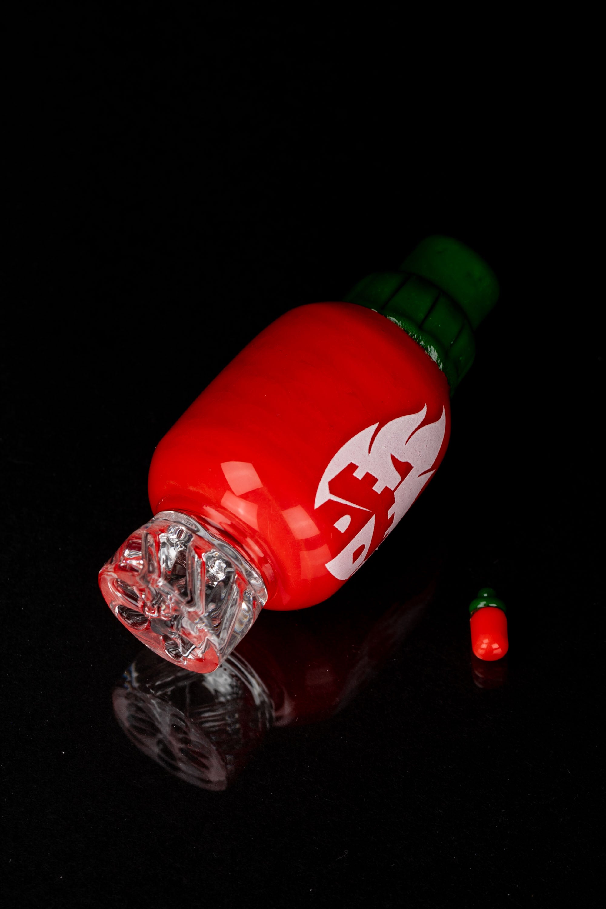 Red glass cannabis water pipe resembling a chili pepper with a clear mouthpiece, against a black background.