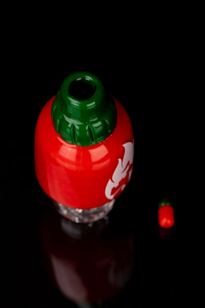 Red strawberry-shaped glass piece with a green leafy top, likely a cannabis water pipe, against a black background.