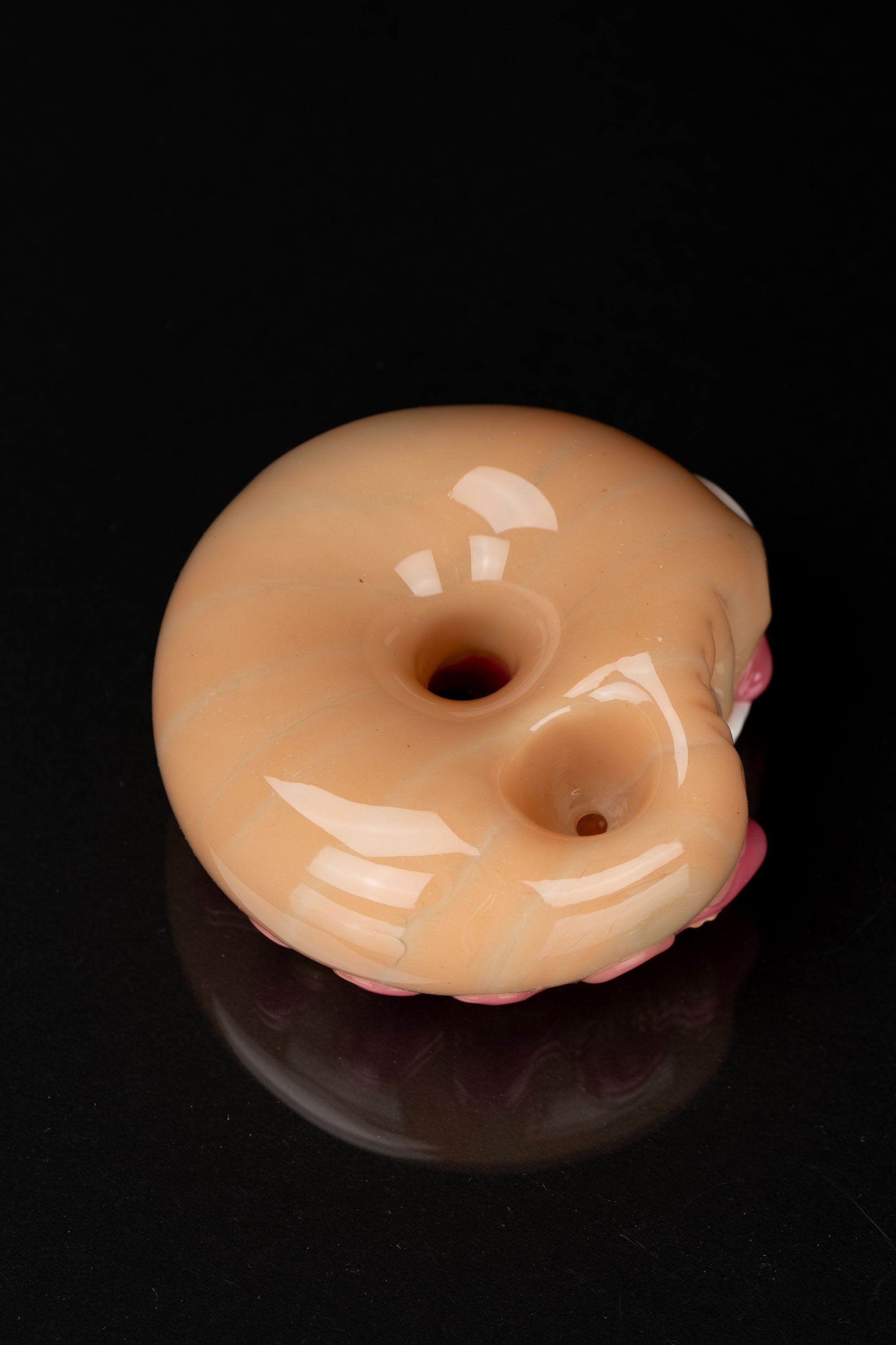 Glass donut-shaped cannabis pipe with white swirls, isolated on black.