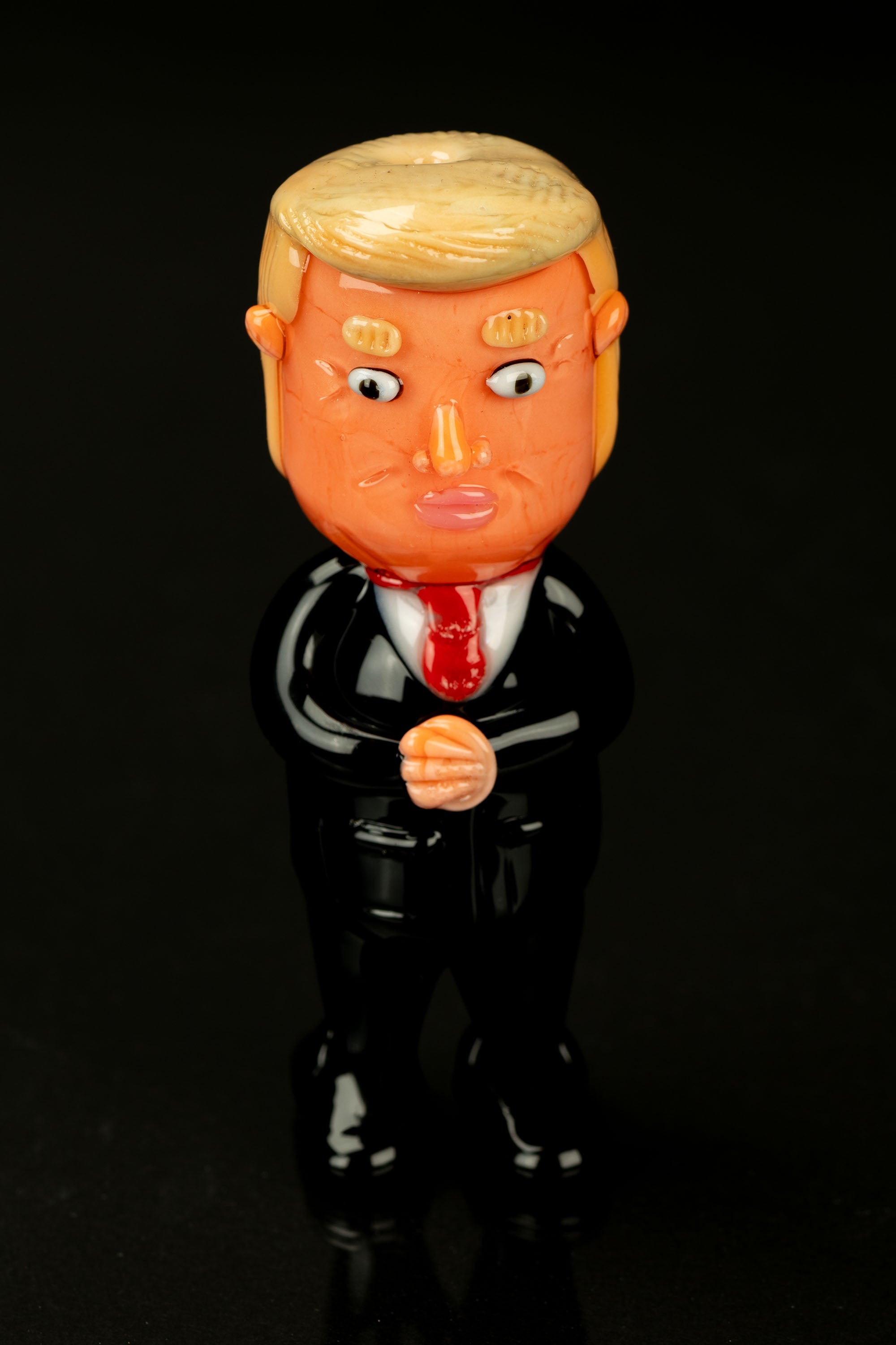 A glossy, cartoonish figurine of Donald Trump in a suit, likely a novelty item related to cannabis accessories.