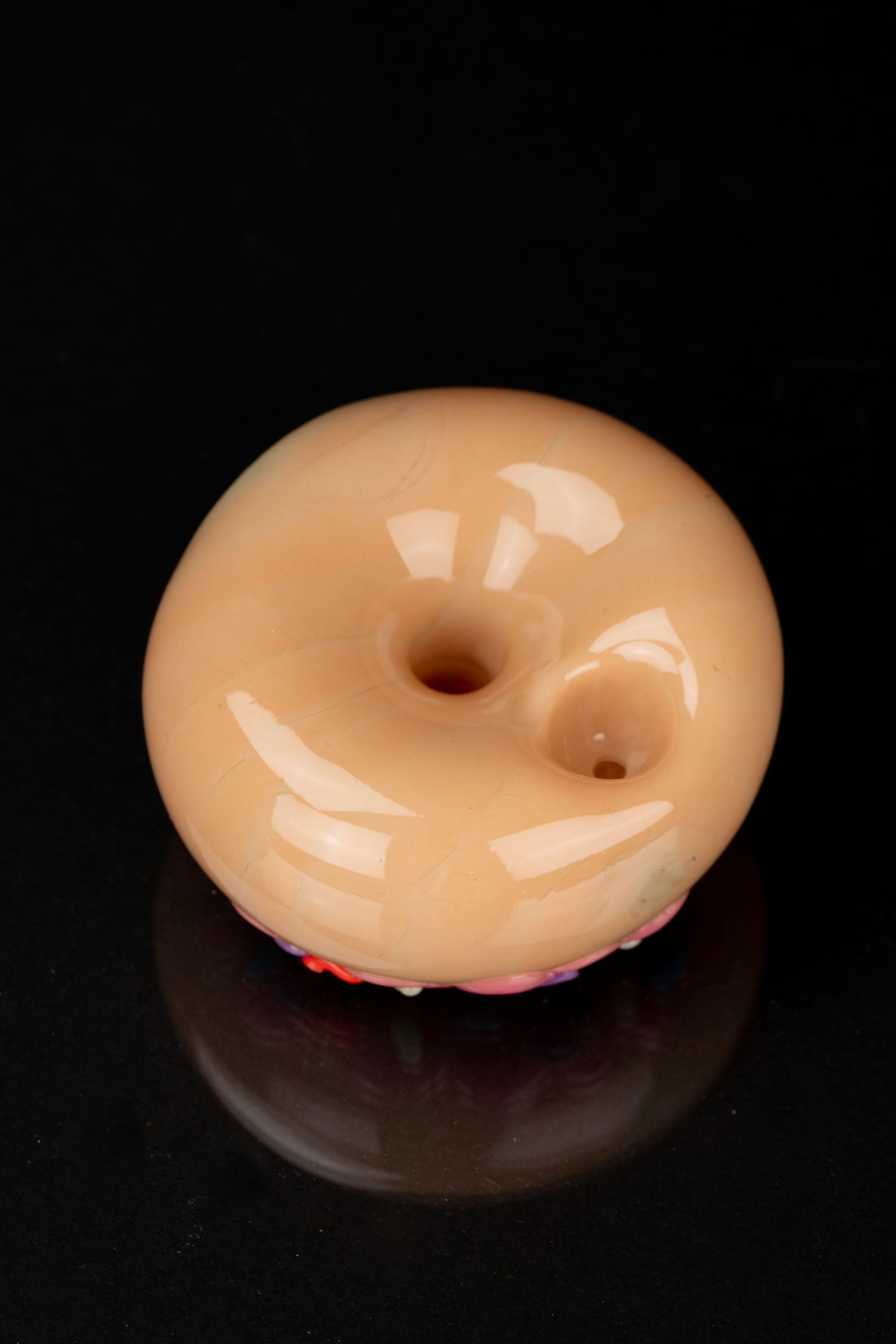Glass donut-shaped cannabis pipe with colorful sprinkles and a reflective black surface.
