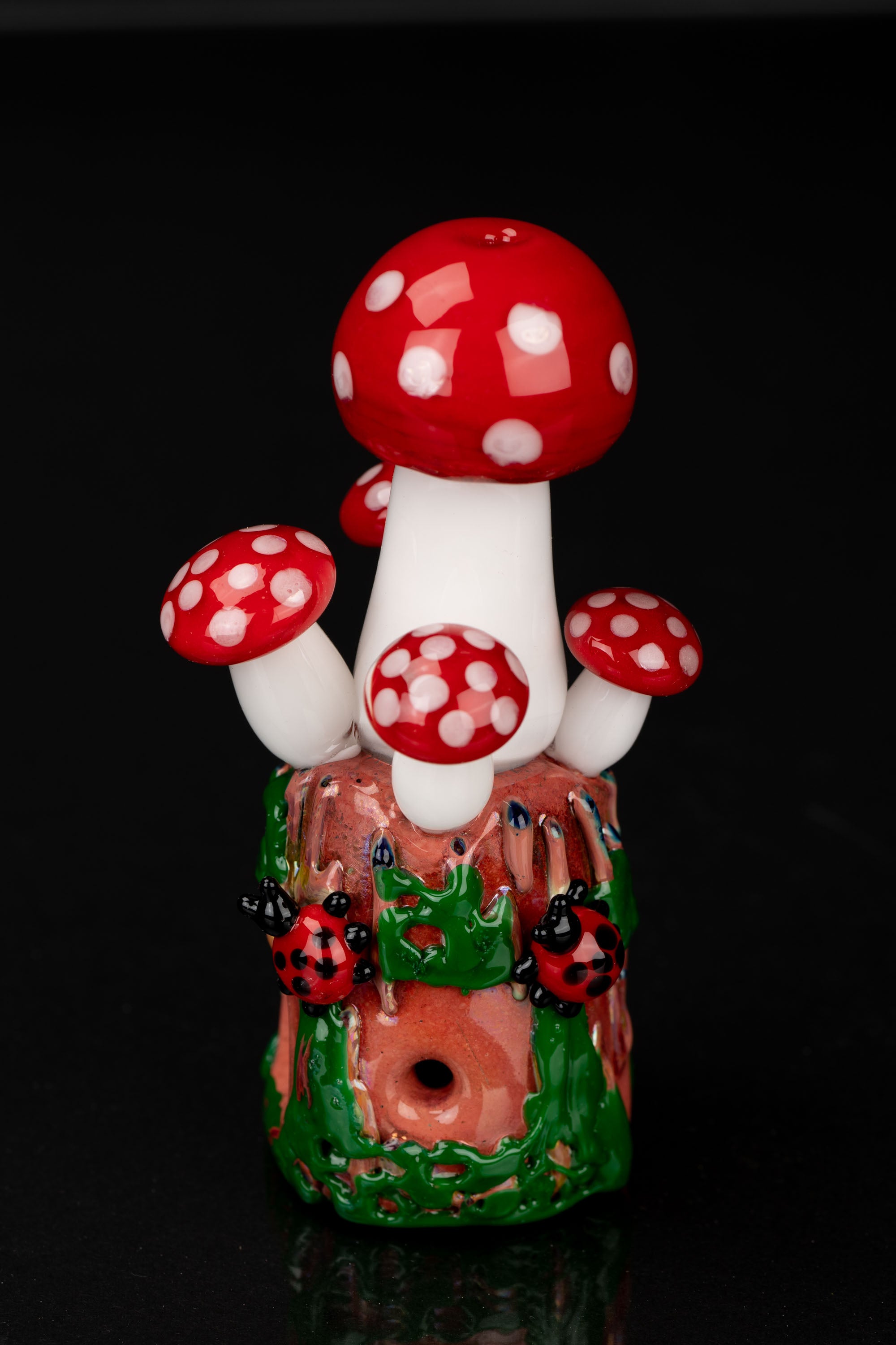 Hand-blown glass mushroom-shaped water pipe with ladybug details on a dark background.