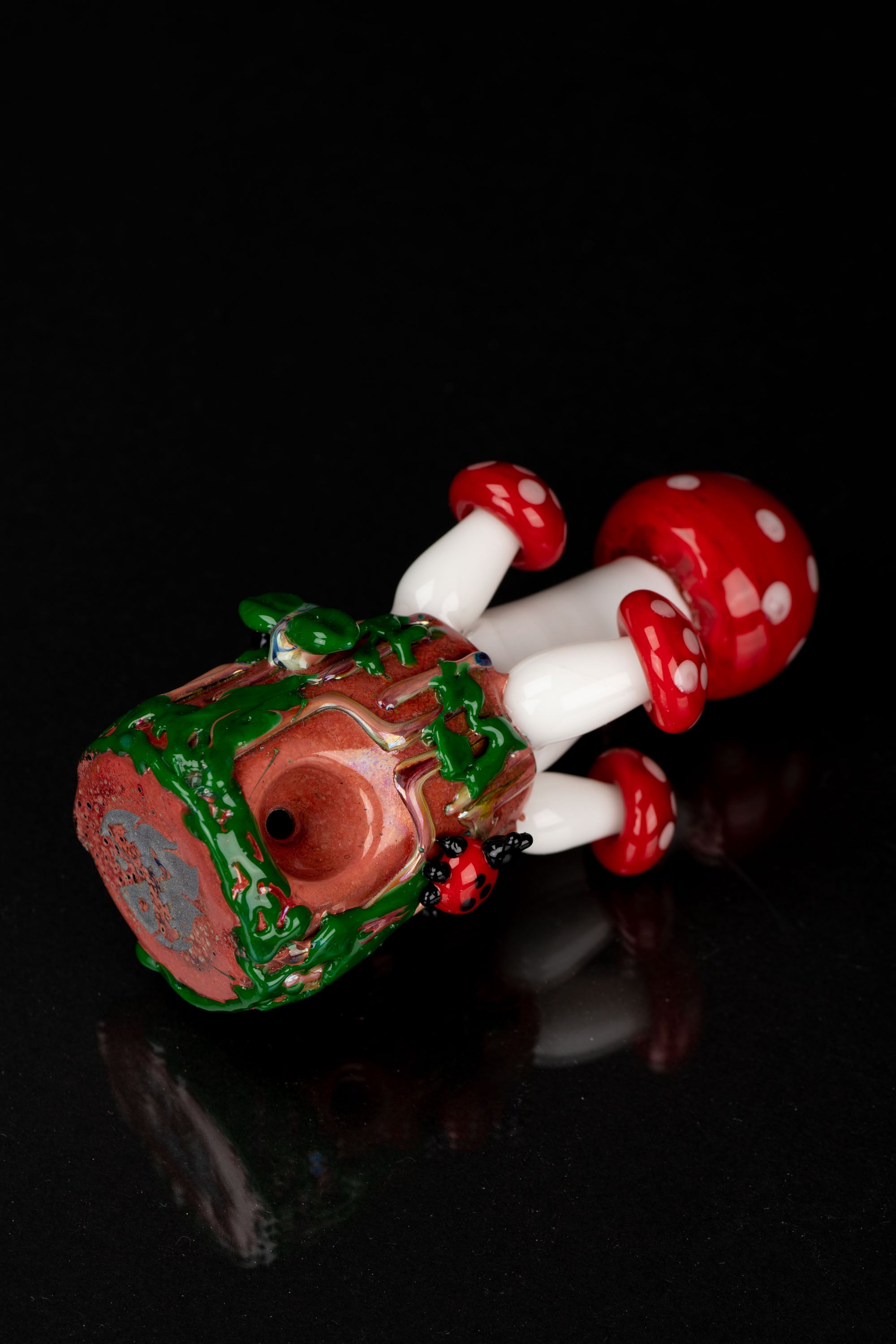 Glass pipe shaped like a mushroom with a red and green speckled base, against a black background.