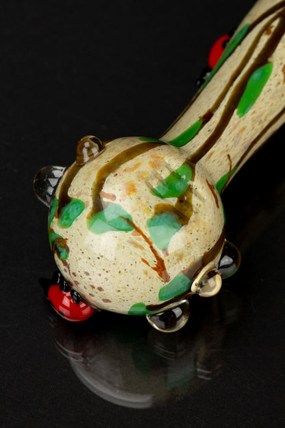 Close-up angled view of the speckled, green-dotted Empire Glassworks Lady Bug Mini Spoon Pipe resting on a reflective black surface.