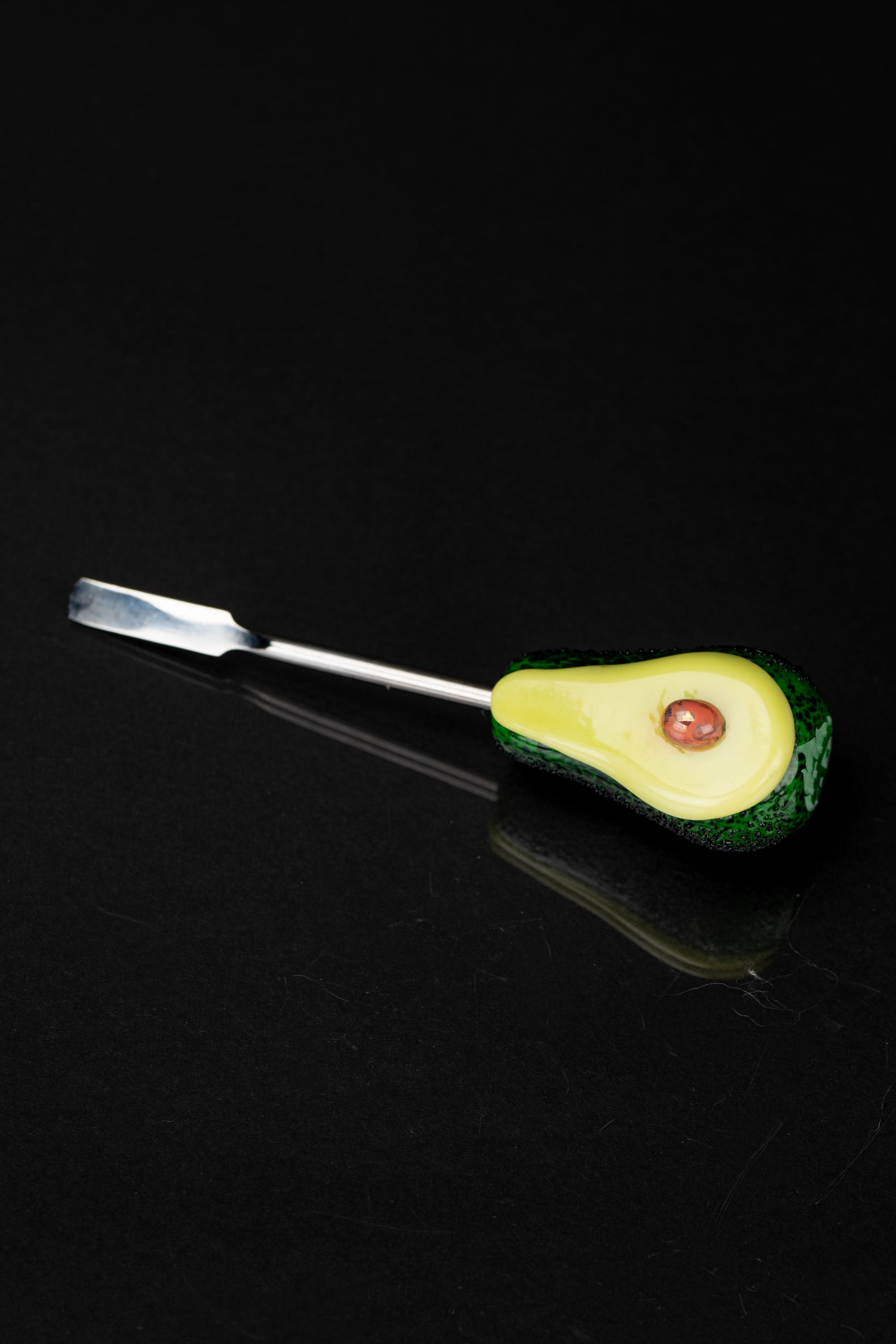 Avocado-shaped dab tool with a metal tip against a black background.
