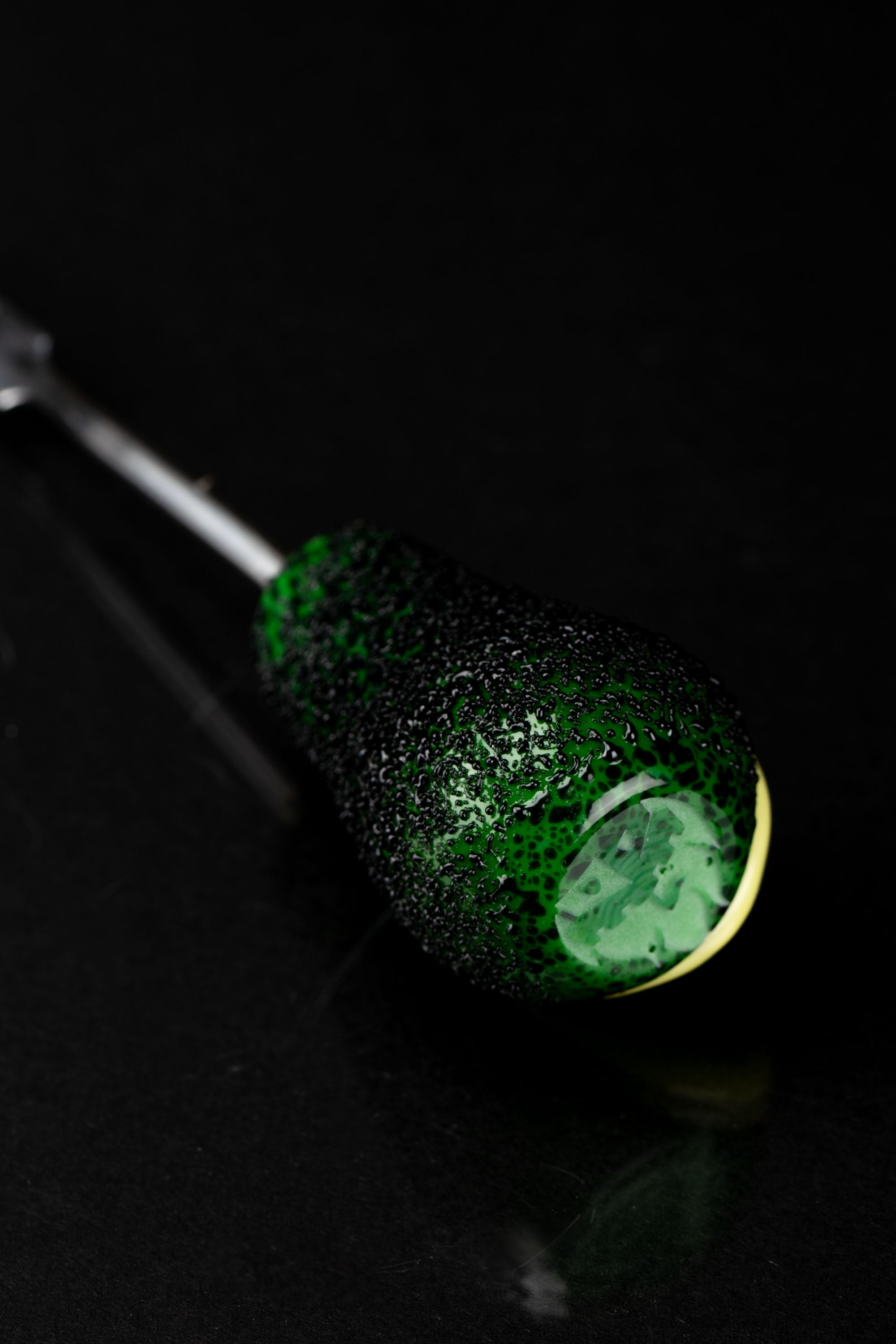 Green-speckled glass pipe against a black background.
