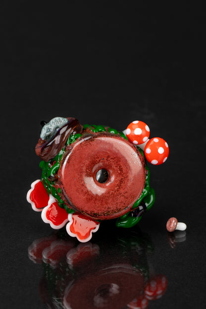 Hand-blown glass pipe shaped like a mushroom with red and white detailing, reflecting on a dark surface.