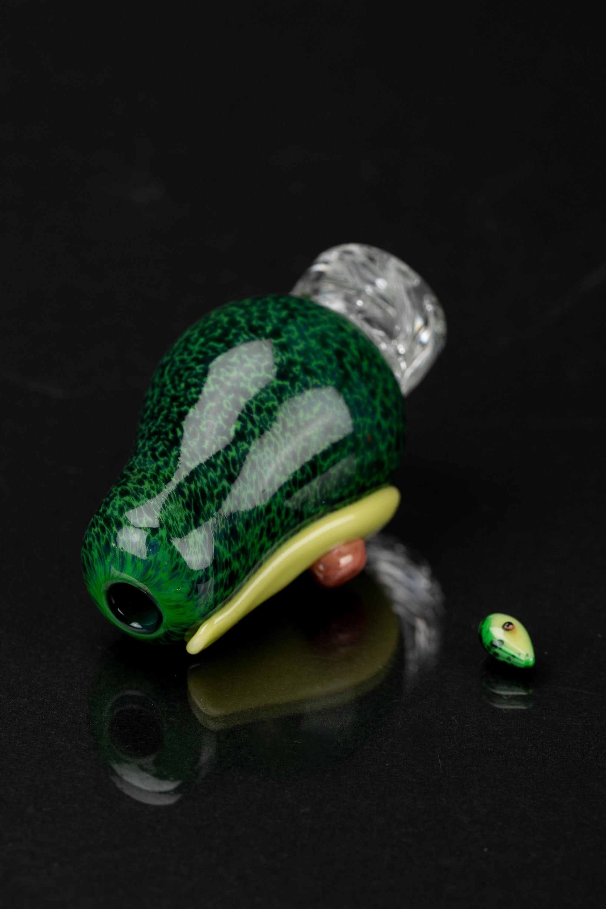 Hand-blown glass avocado-shaped oil rig attachment with a matching carb cap, displayed on a reflective black surface.