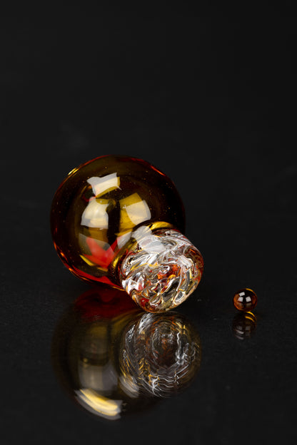 Artistic studio shot of a colorful glass cannabis water pipe reflecting on a dark surface.