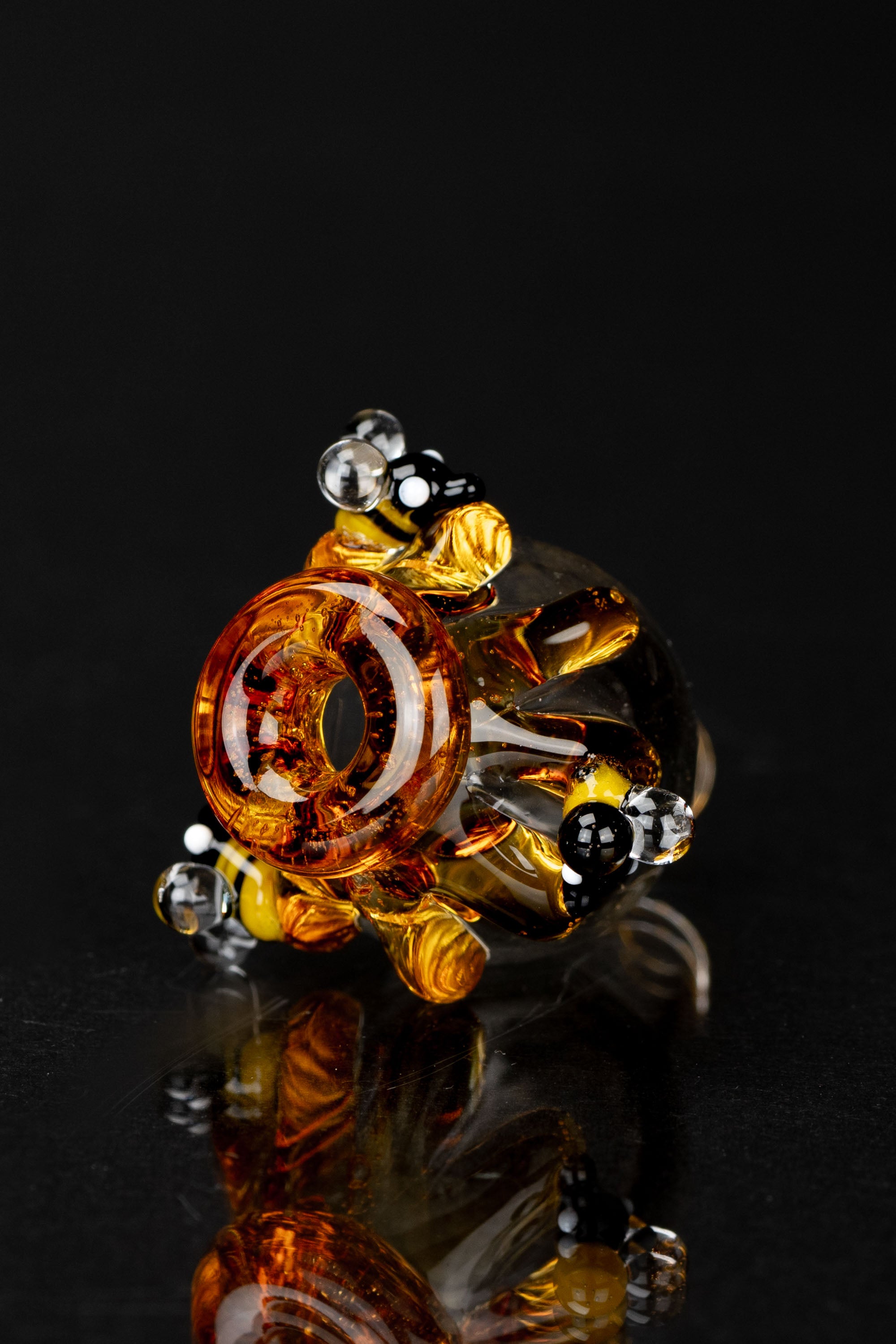 Hand-blown glass cannabis pipe with amber and black accents, displayed on a reflective black surface.
