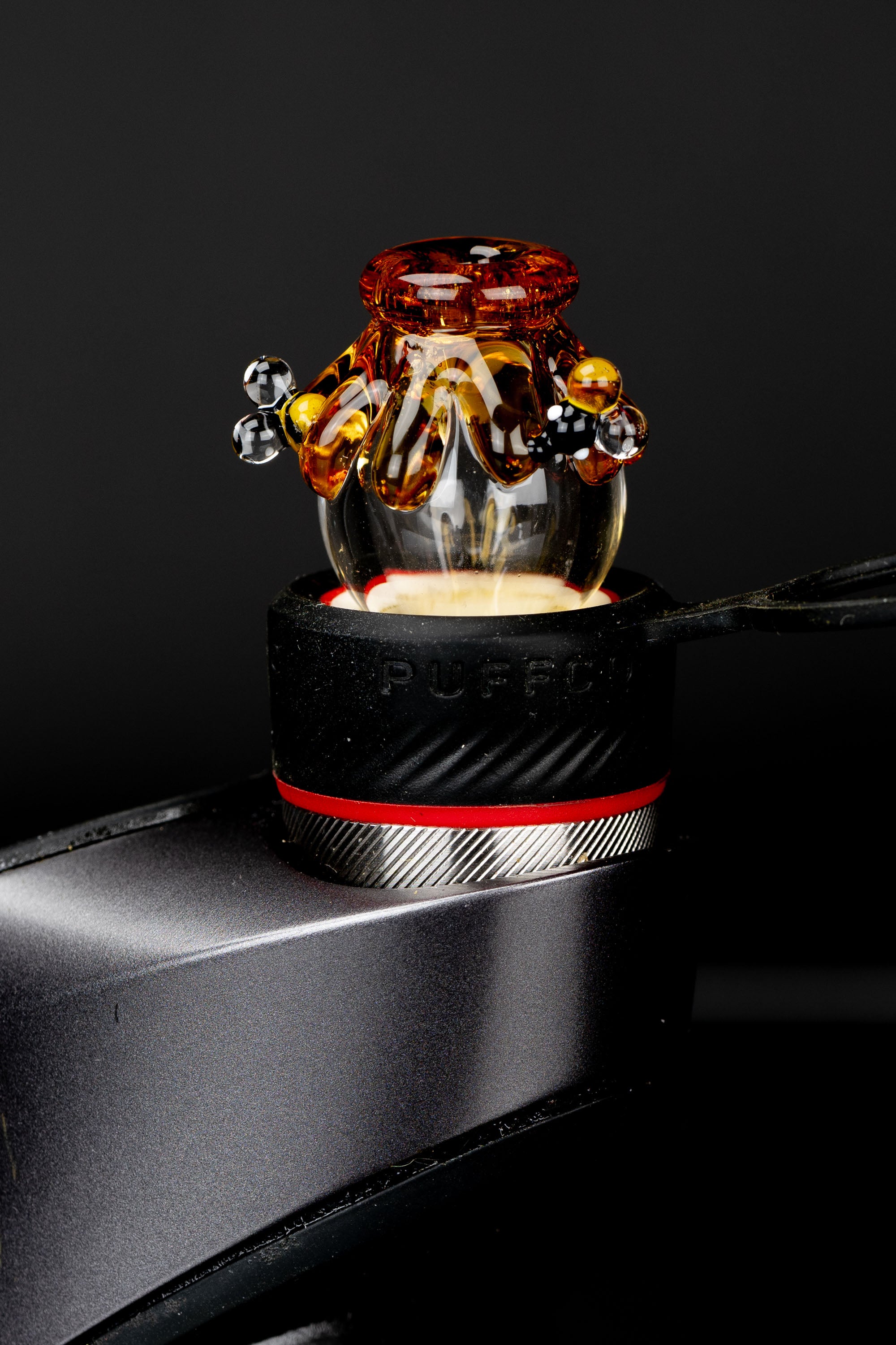 Amber glass cannabis oil rig atop a black metal surface, studio shot.