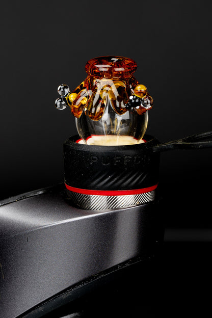 Amber glass cannabis oil rig atop a black metal surface, studio shot.