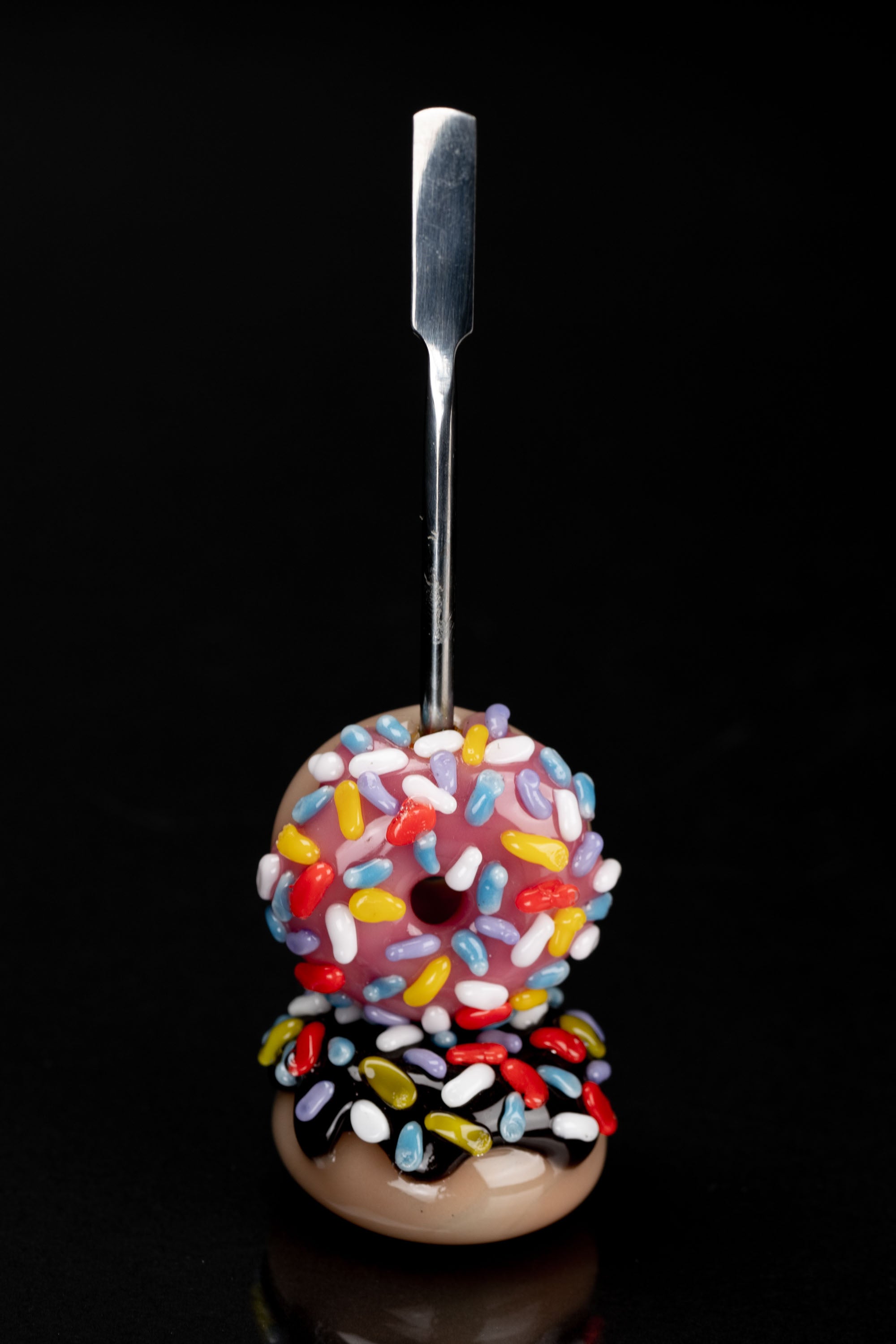 Glass dab rig shaped like a sprinkle-covered donut with a titanium tool inserted into the center.