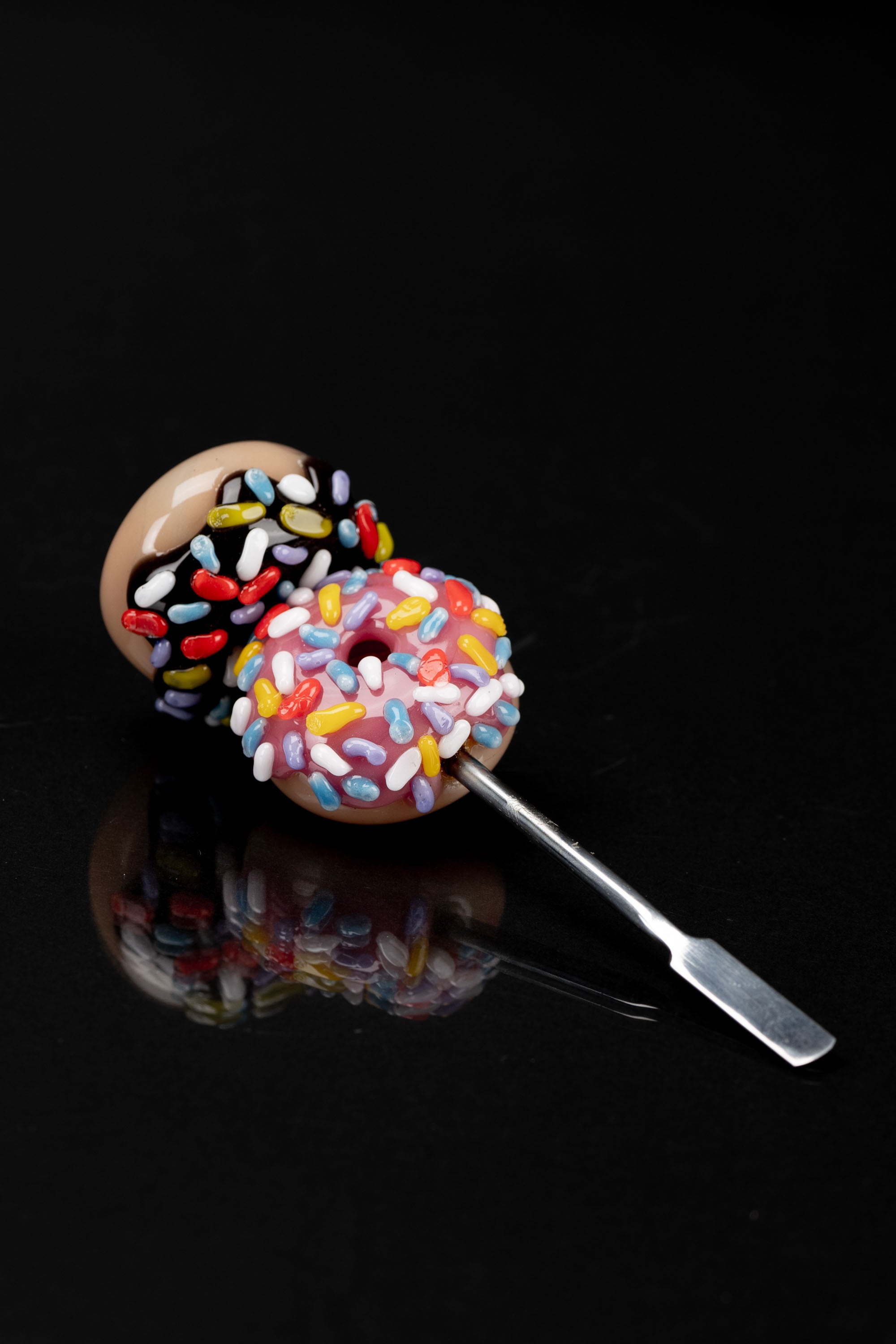 Glass dab tool shaped like a sprinkled donut, reflecting on a black surface.