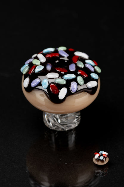 A colorful, hand-blown glass cap resembling a sprinkle-covered donut, likely used as a cannabis accessory.