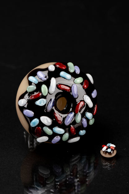 Glass cannabis pipe shaped like a sprinkled donut, against a black background.