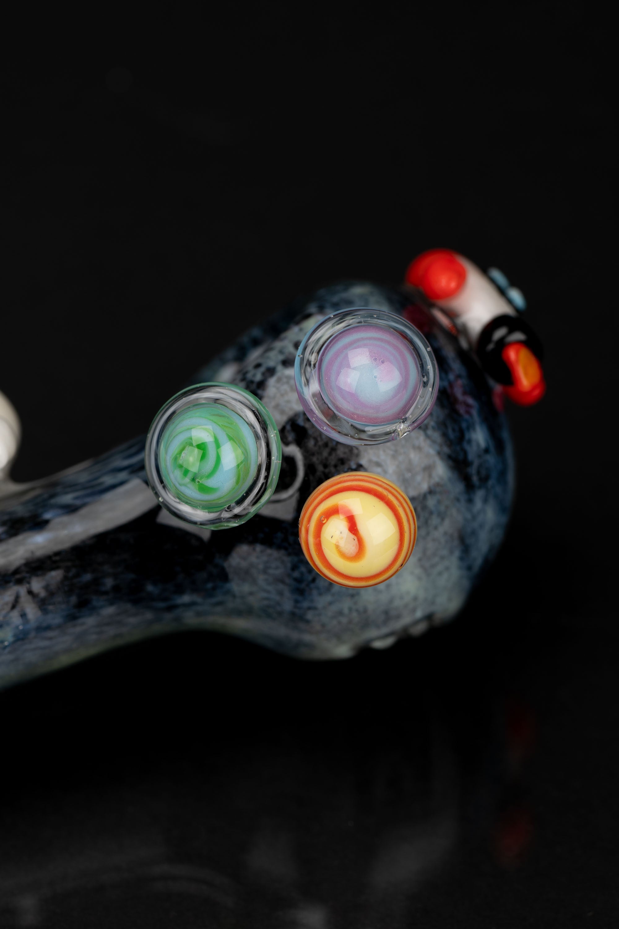 A close-up of a colorful glass cannabis pipe with multiple bowls against a black background.