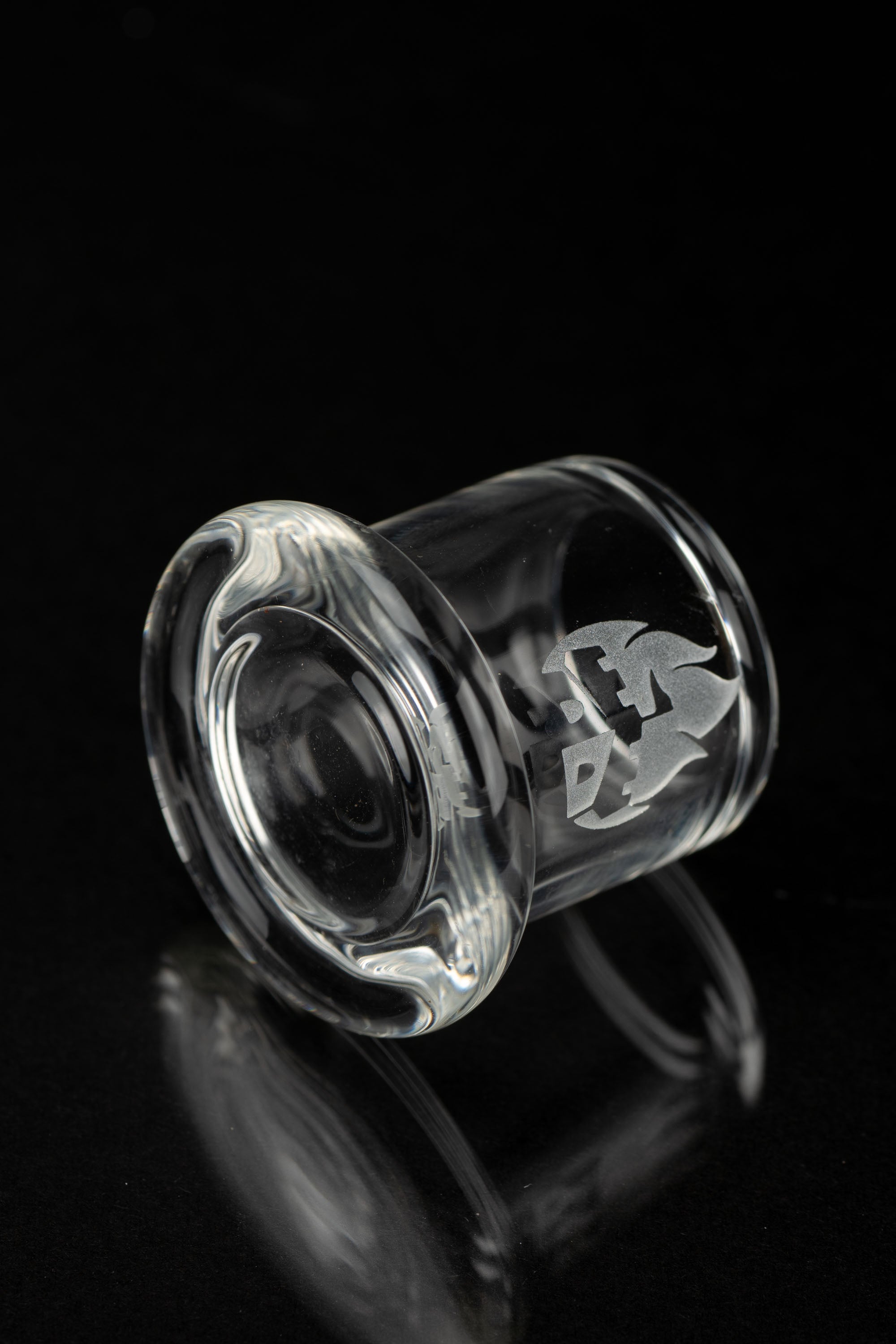 Clear glass cannabis concentrate container with etched logo, isolated on black.