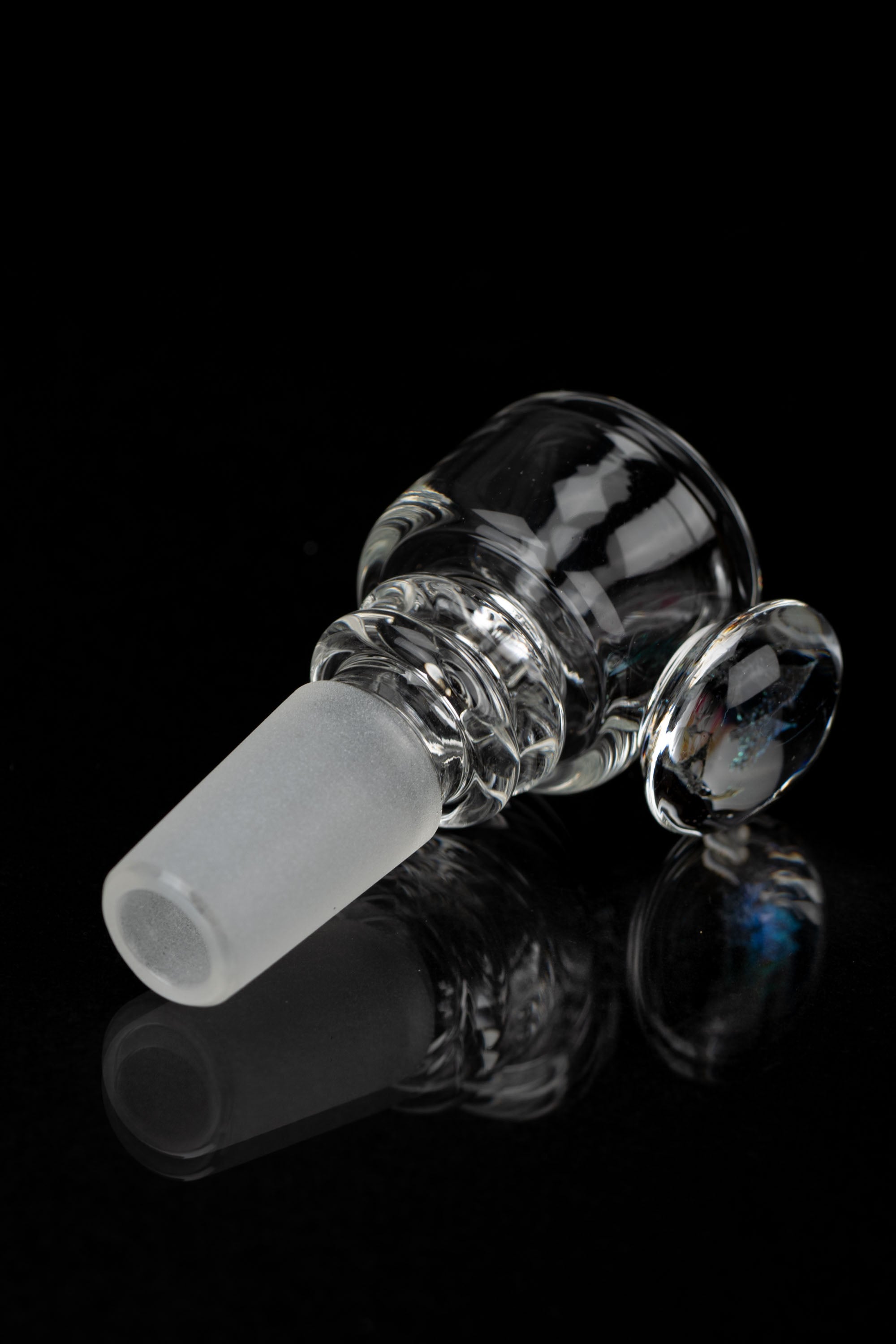 Clear glass cannabis bowl with intricate swirling patterns, reflecting on a black surface.