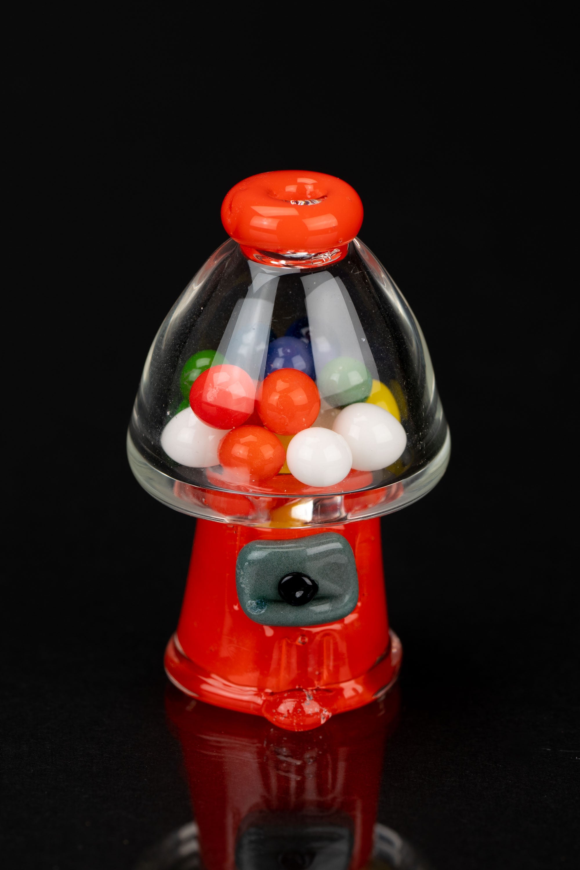 Red glass gumball machine filled with colorful spheres, likely a cannabis accessory.