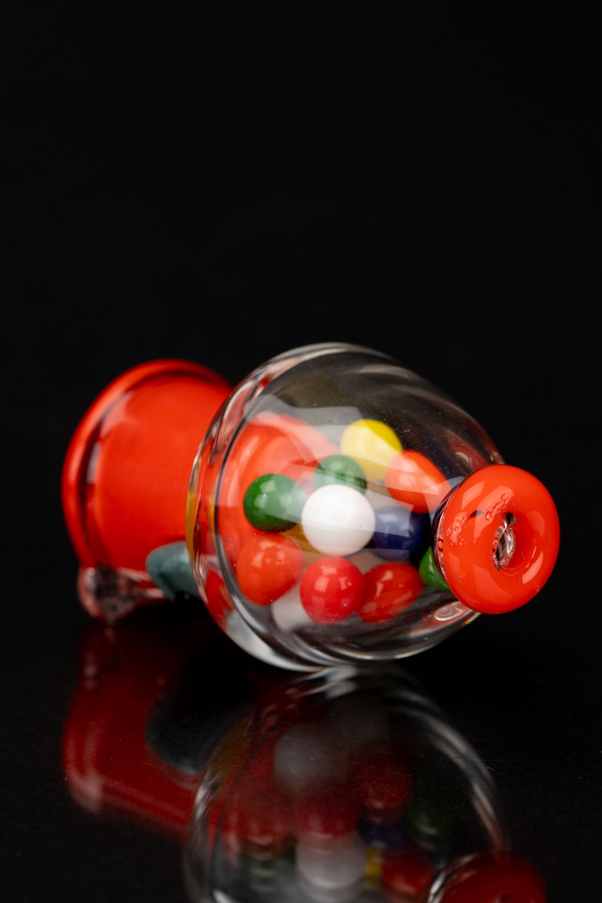 Red glass bubbler filled with colorful cannabis concentrates, reflecting on a glossy surface.