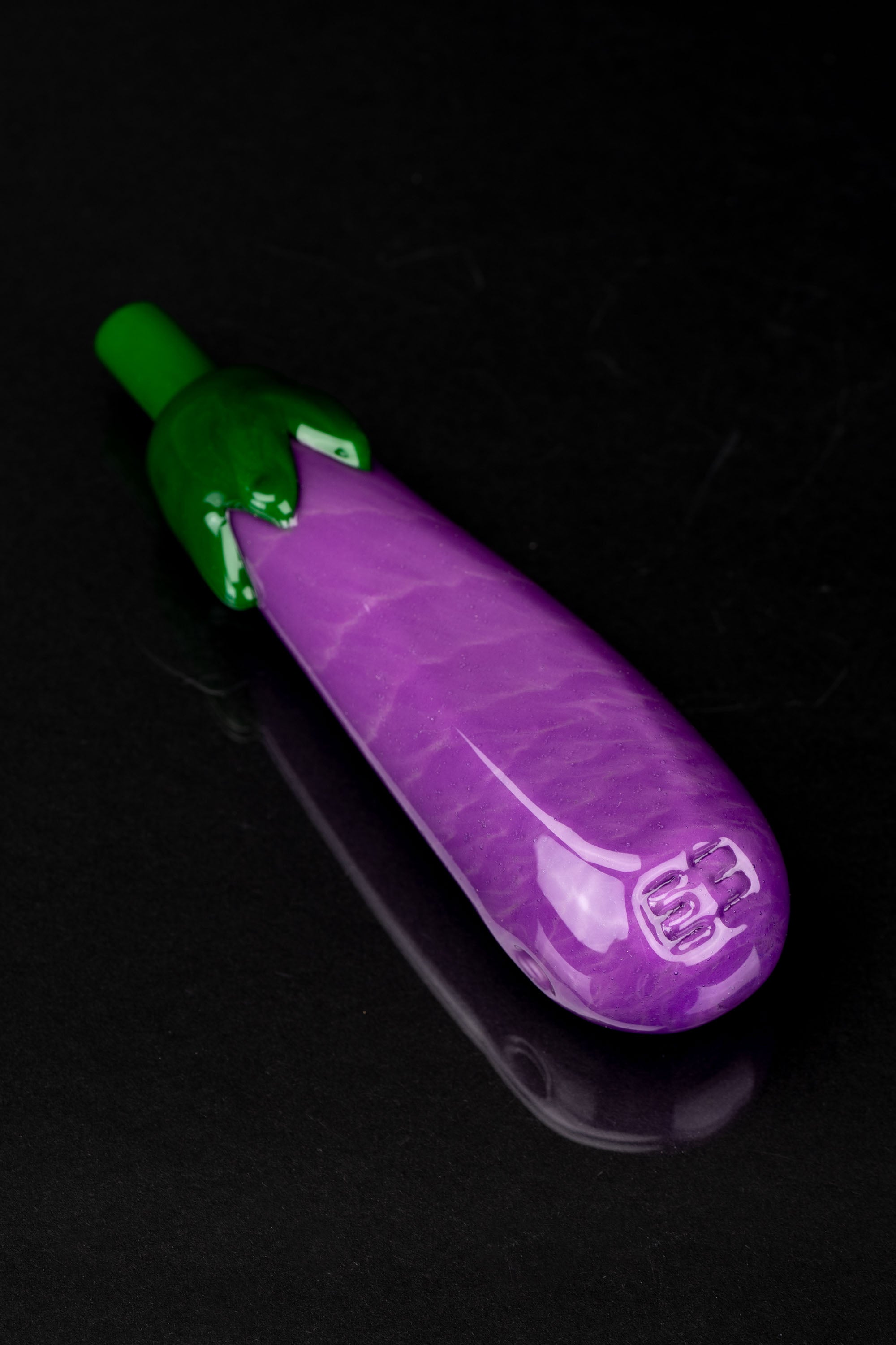 Purple glass pipe shaped like an eggplant with a green mouthpiece, against a black background.
